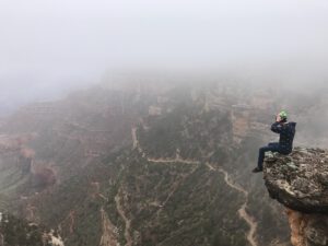 a man sits at the edge of a vast cliff